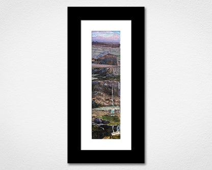 Framed artwork of a landscape with mountains and a lake on a white wall.