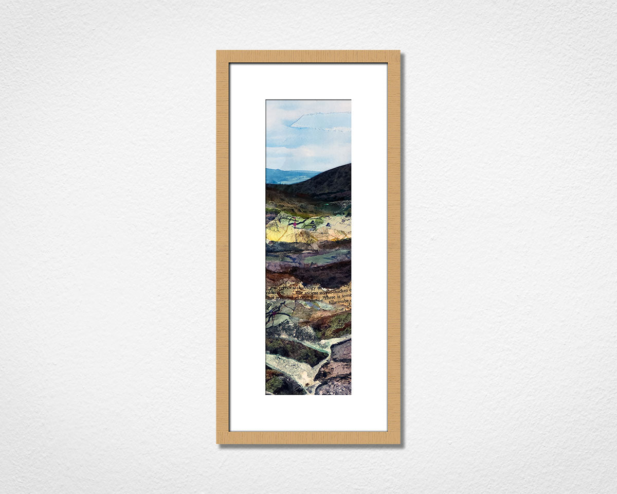 Framed landscape print of a mountainous scene of Dartmoor National Park with a wooden oak frame on a white wall.