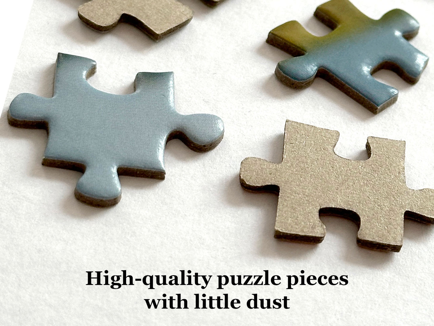 Several puzzle pieces on a white surface, including two painted pieces in muted blue-gray and tan tones, with the text 'High-quality puzzle pieces with little dust' at the bottom.