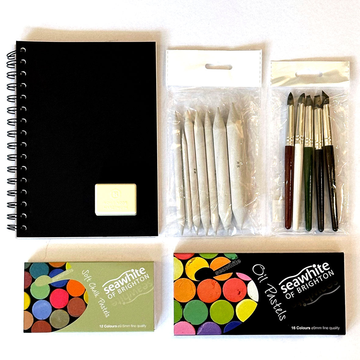 The Pastels Kit Box containing art supplies including a black notebook, pastels, and drawing tools on a white background