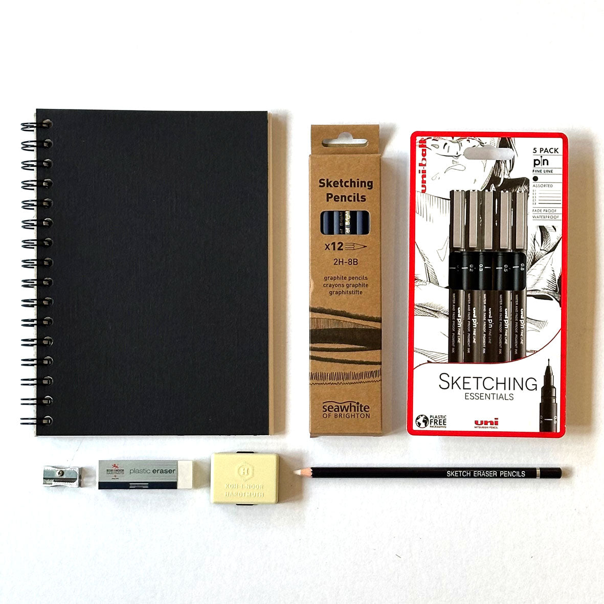 The Sketching Kit Box containing art supplies including a black notebook, sketching pencils, and a pencil eraser on a white background.